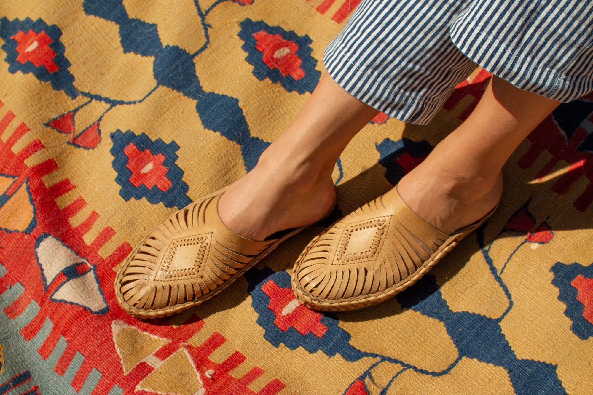 Female wearing natural leather slip-on sandals with hand-woven diamond centerpiece on colorful rug