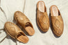 Two pairs of natural leather slip-on sandals with hand-woven diamond centerpiece on white linen