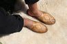Male wearing natural leather slip-on sandals with hand-woven diamond centerpiece on shearling rug